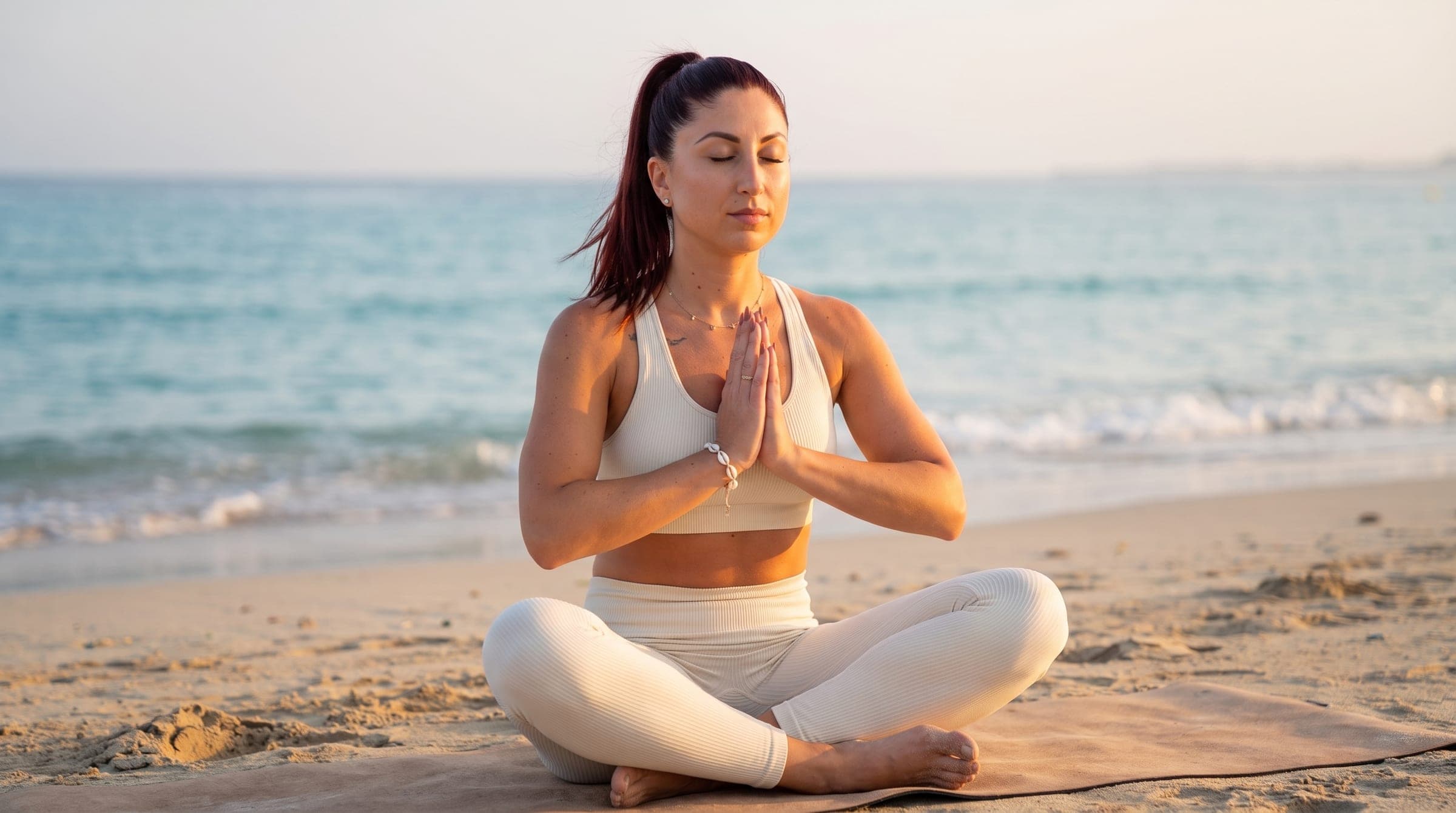 Frau sitzt am Strand in ruhiger Meditation, die Hände vor der Brust