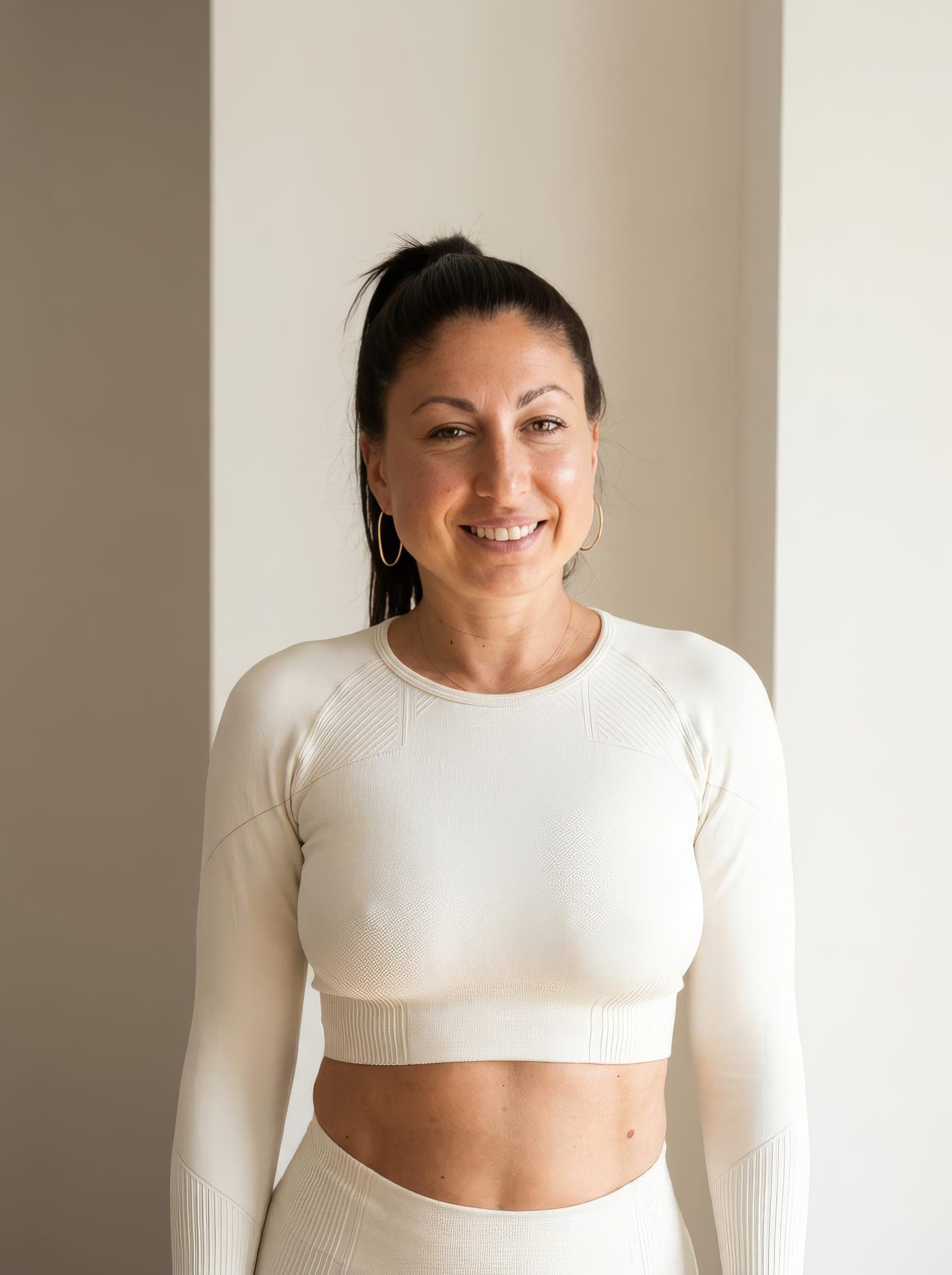 Porträt von Angel: lächelnde Trainerin mit dunklem Pferdeschwanz in heller Sportkleidung